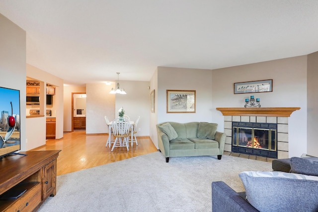 living room featuring light colored carpet, light wood-style flooring, an inviting chandelier, a tile fireplace, and baseboards