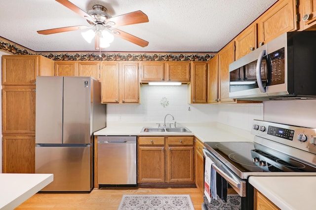 kitchen with stainless steel appliances, light countertops, light wood-style flooring, a sink, and a textured ceiling