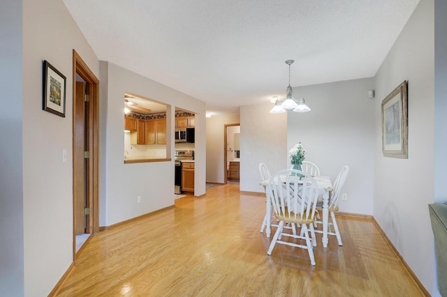 dining area with a textured ceiling, light wood-style flooring, baseboards, and an inviting chandelier