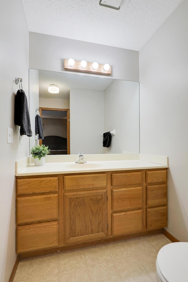 bathroom featuring toilet, a textured ceiling, vanity, and baseboards