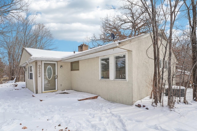 view of front of home with a chimney, central AC, and stucco siding