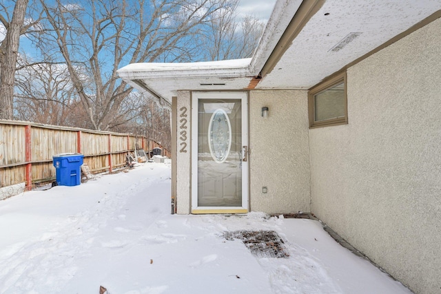 snow covered property entrance featuring fence and stucco siding