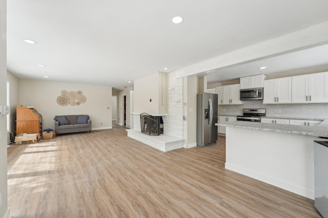 kitchen with stainless steel appliances, white cabinetry, light wood-style floors, open floor plan, and decorative backsplash