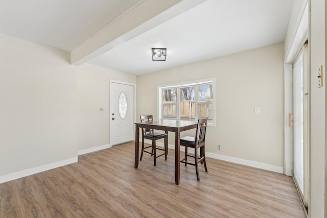 dining area featuring light wood-style flooring, baseboards, and beam ceiling