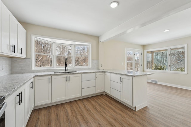 kitchen featuring a peninsula, light wood finished floors, visible vents, and a sink