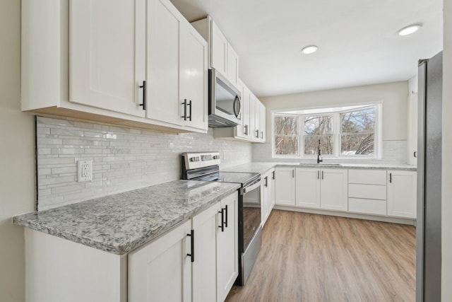 kitchen featuring appliances with stainless steel finishes, light wood-type flooring, white cabinetry, and a sink