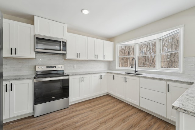 kitchen featuring stainless steel appliances, light wood-type flooring, white cabinets, and a sink