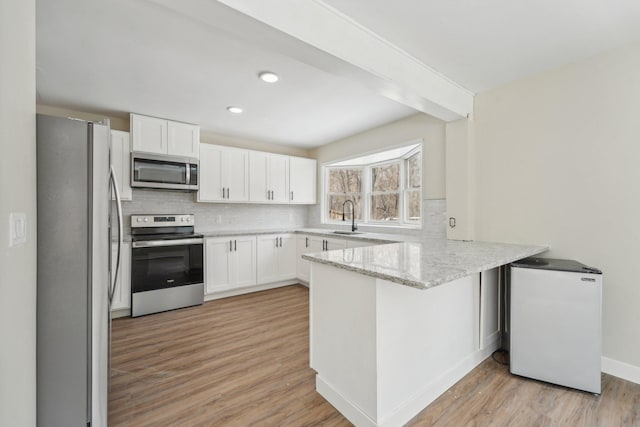 kitchen with stainless steel appliances, backsplash, a sink, and a peninsula