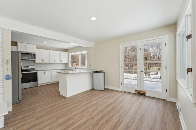 kitchen with tasteful backsplash, light wood-style flooring, appliances with stainless steel finishes, white cabinetry, and a peninsula