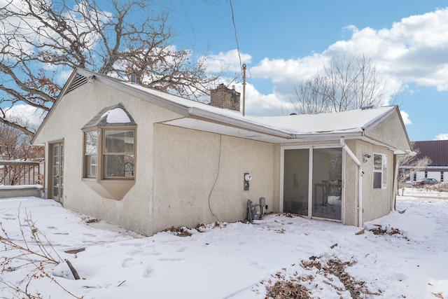 snow covered back of property featuring a chimney and stucco siding