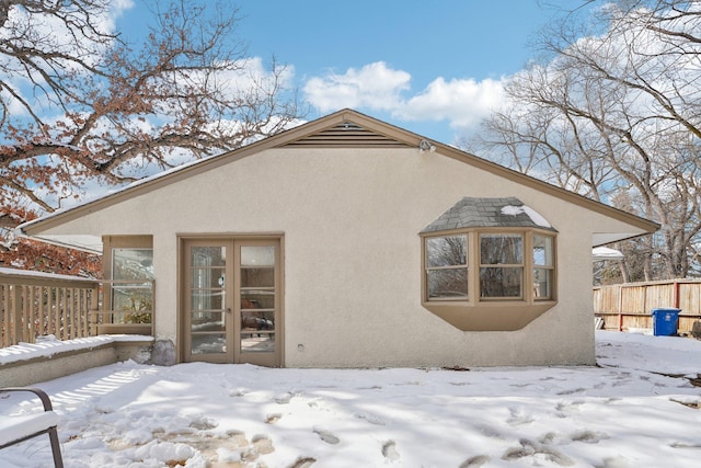 snow covered property featuring fence, french doors, and stucco siding