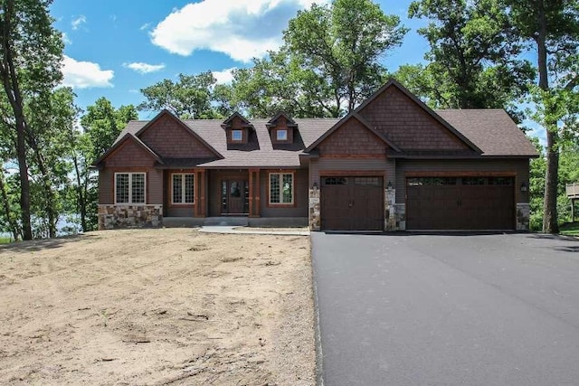 craftsman house with an attached garage, stone siding, and aphalt driveway