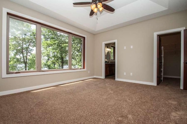 carpeted spare room with a tray ceiling, a ceiling fan, and baseboards