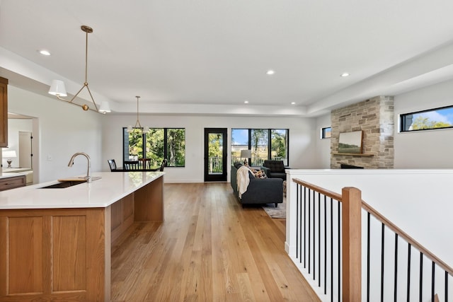 kitchen with light countertops, light wood-style flooring, brown cabinets, a stone fireplace, and a sink