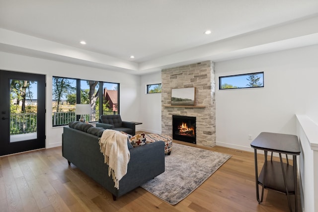 living area with a raised ceiling, a fireplace, light wood-style flooring, baseboards, and recessed lighting
