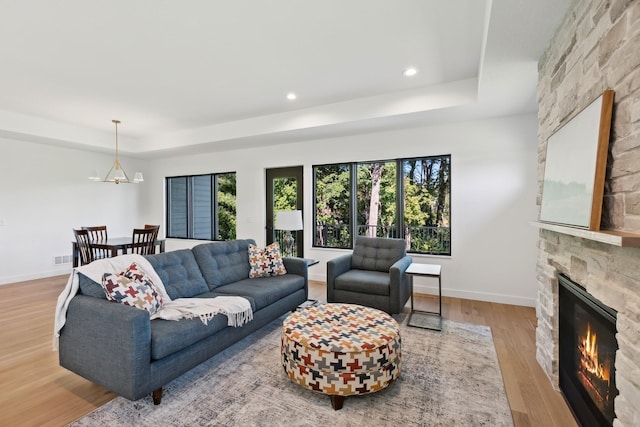 living area with a stone fireplace, baseboards, wood finished floors, and a tray ceiling