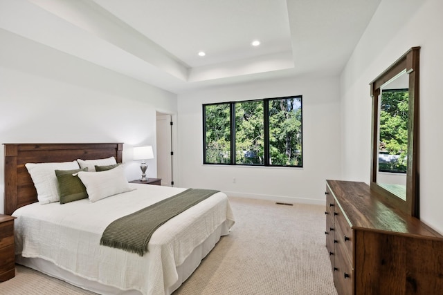 bedroom featuring a tray ceiling, multiple windows, light colored carpet, and baseboards