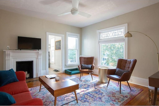 living area with a wealth of natural light, ceiling fan, baseboards, and wood finished floors