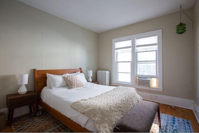 bedroom with radiator, cooling unit, baseboards, and wood finished floors