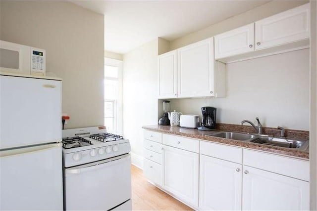 kitchen featuring stone countertops, white appliances, a sink, white cabinets, and light wood finished floors