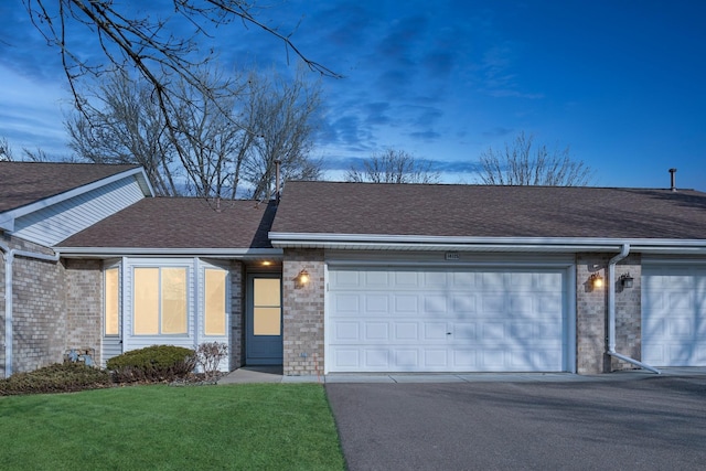 view of front facade featuring aphalt driveway, a garage, brick siding, roof with shingles, and a front lawn