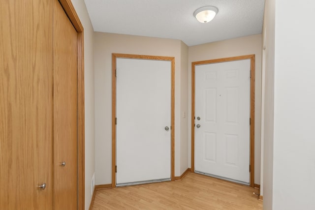 doorway to outside featuring baseboards, a textured ceiling, and light wood finished floors