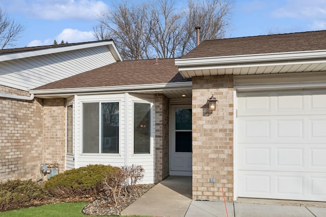 view of exterior entry with brick siding, roof with shingles, and an attached garage