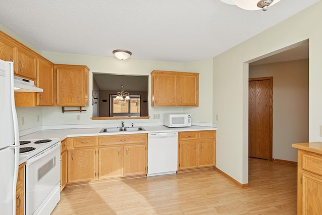 kitchen with white appliances, light countertops, light wood-type flooring, under cabinet range hood, and a sink