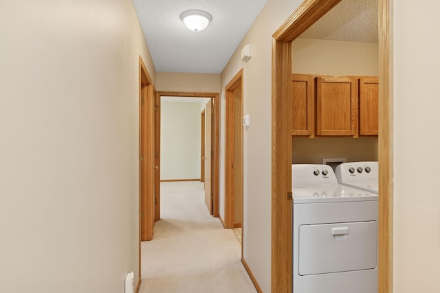 clothes washing area with light colored carpet, cabinet space, a textured ceiling, independent washer and dryer, and baseboards