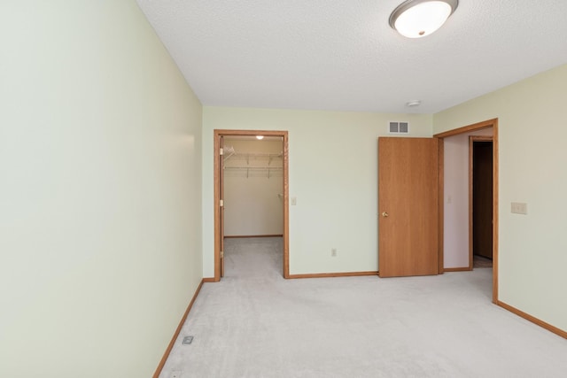 unfurnished bedroom featuring a textured ceiling, light carpet, visible vents, baseboards, and a spacious closet