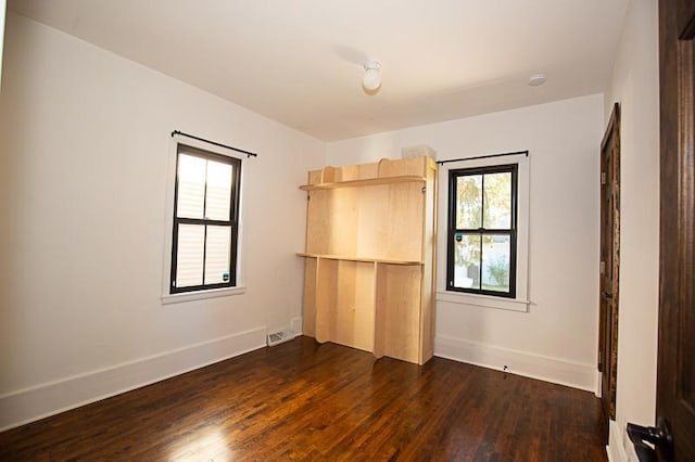 empty room featuring baseboards, visible vents, and dark wood-style flooring