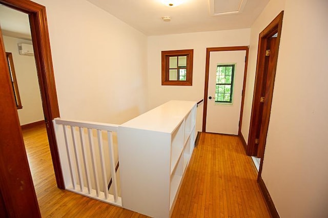 hallway with baseboards, a wall mounted air conditioner, an upstairs landing, and light wood-style floors