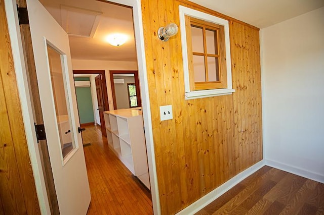 hallway featuring baseboards, wood finished floors, and wooden walls