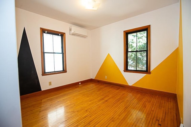 empty room featuring light wood-type flooring, baseboards, and a wall mounted AC