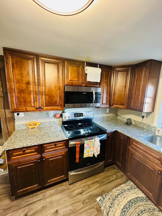 kitchen with stainless steel appliances, light wood-type flooring, a sink, and light stone countertops