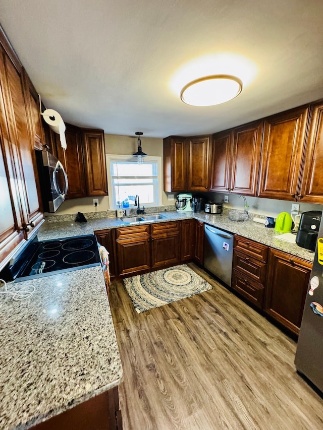 kitchen with light wood-type flooring, light stone counters, stainless steel appliances, and a sink