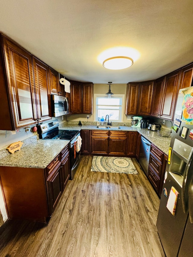 kitchen featuring light stone countertops, light wood-style flooring, stainless steel appliances, and a sink