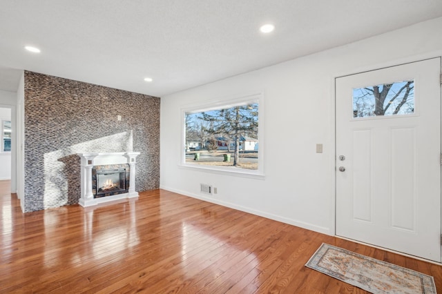 unfurnished living room with visible vents, plenty of natural light, a glass covered fireplace, and hardwood / wood-style flooring