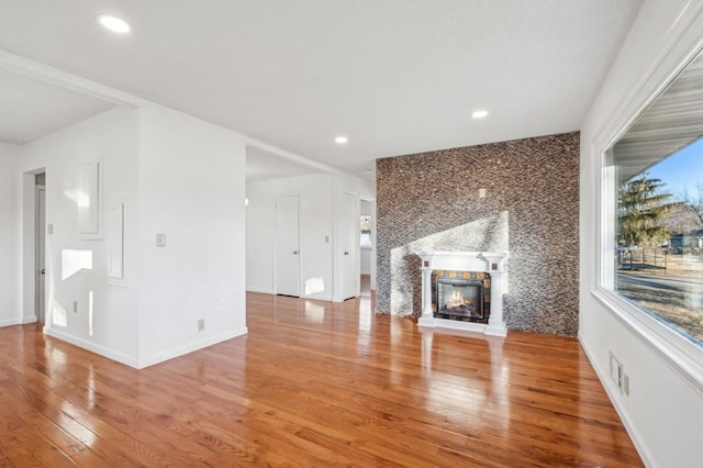 unfurnished living room with recessed lighting, baseboards, wood finished floors, and a glass covered fireplace