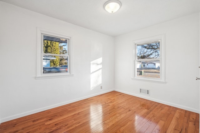 unfurnished room with baseboards, visible vents, and hardwood / wood-style floors