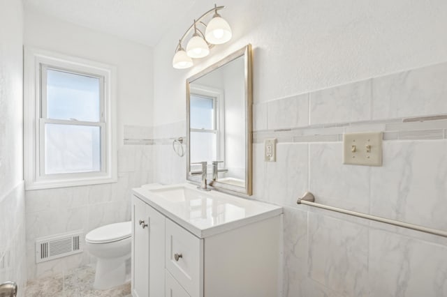 half bathroom featuring toilet, vanity, visible vents, tile walls, and marble finish floor