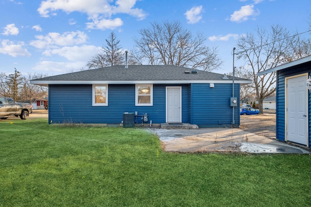 back of property featuring roof with shingles, a lawn, and central AC