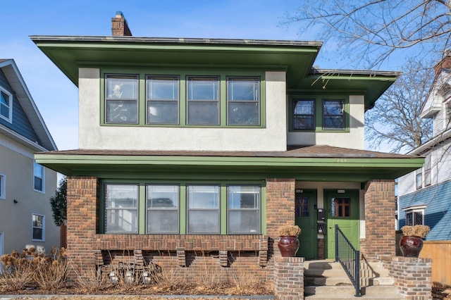 view of front of home featuring brick siding, a chimney, and stucco siding