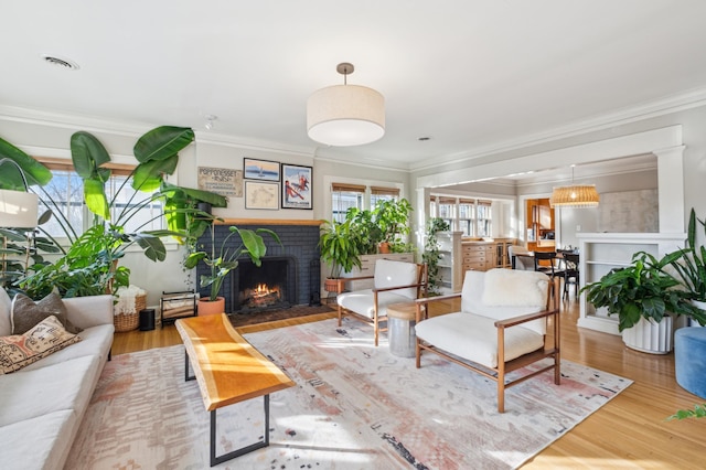 living room featuring a brick fireplace, crown molding, and wood finished floors