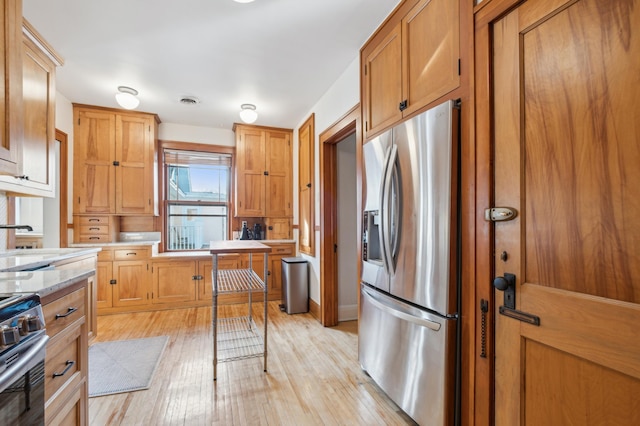 kitchen featuring appliances with stainless steel finishes, brown cabinetry, a sink, and light wood-style floors