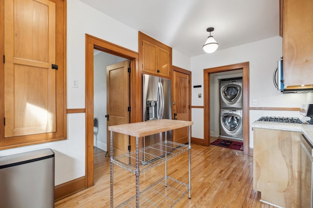 kitchen featuring light wood finished floors, baseboards, appliances with stainless steel finishes, stacked washer / drying machine, and light countertops