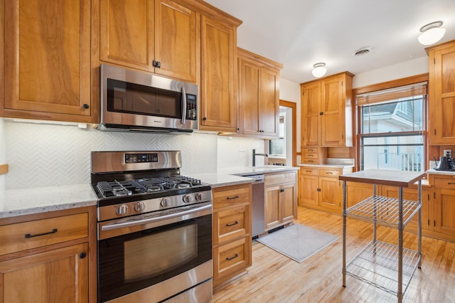 kitchen featuring appliances with stainless steel finishes, light wood-style flooring, tasteful backsplash, and light stone countertops