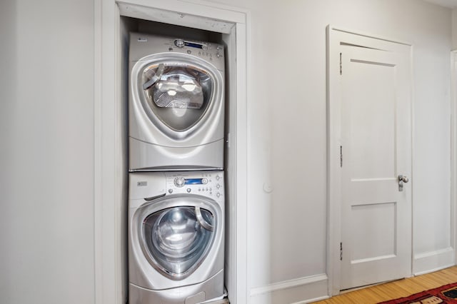 laundry area with stacked washer and clothes dryer, baseboards, and wood finished floors