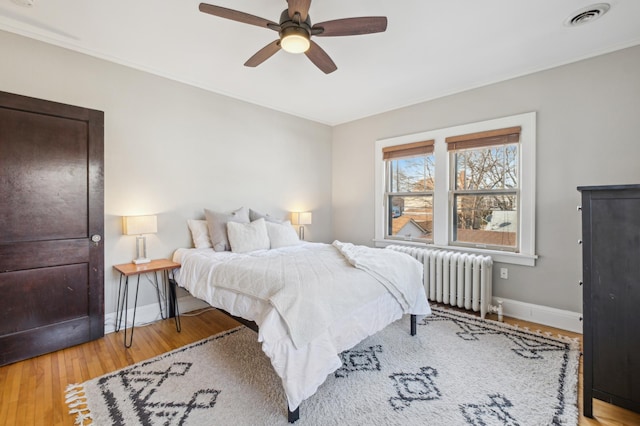 bedroom featuring radiator heating unit, baseboards, wood finished floors, a ceiling fan, and crown molding