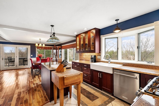 kitchen featuring decorative light fixtures, glass insert cabinets, stainless steel dishwasher, and a sink